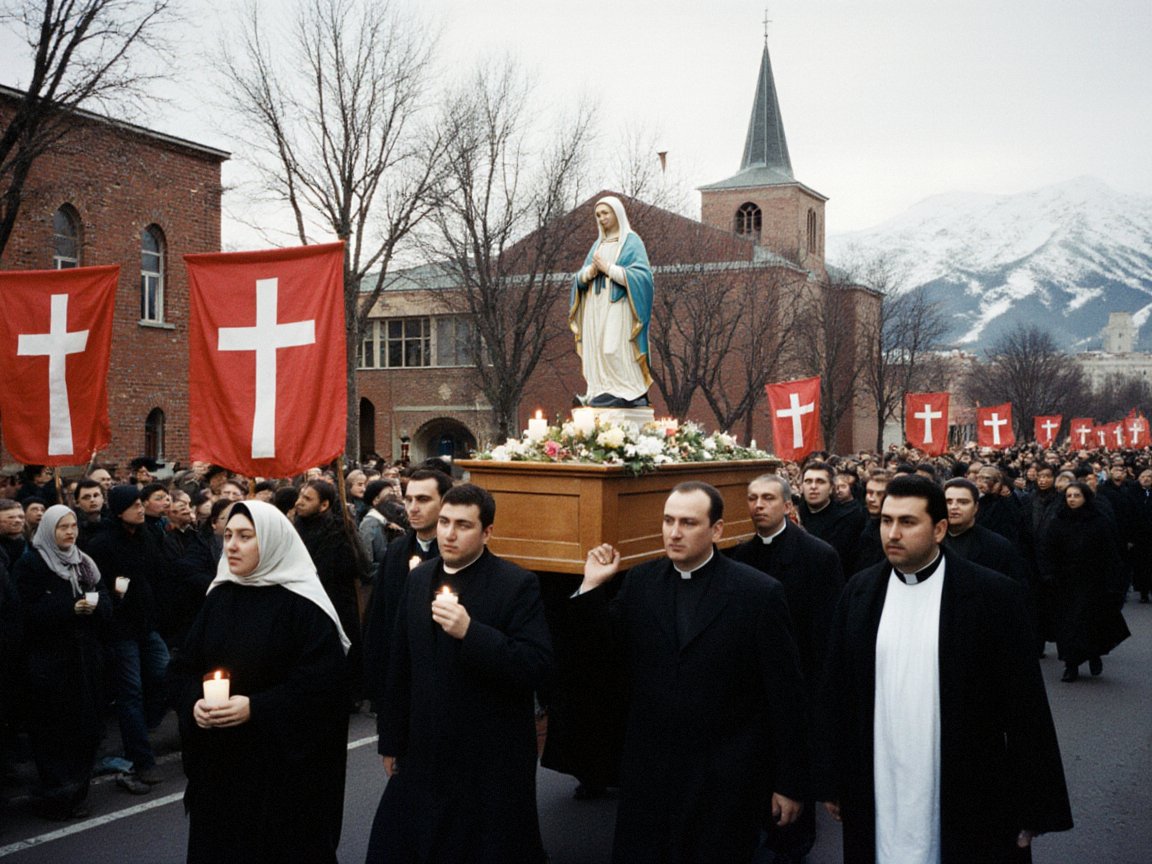 Priests in black cassocks carry a statue of the Virgin Mary on a flower-covered wooden litter down a street, followed by a large crowd with candles and crimson banners bearing white crosses, past a brick church with a spire and a snowy mountain